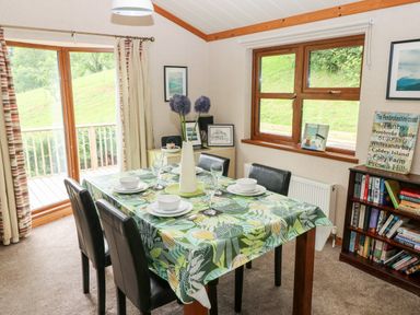 A dining room with a table set for four near windows and a bookshelf at The Beeches in Narberth