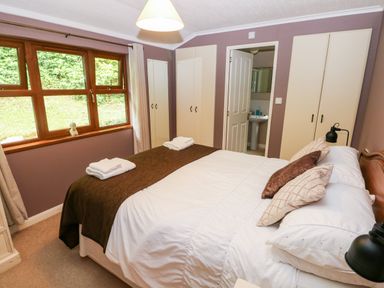 A bedroom with a bed with pillows and folded towels a window with curtains and wardrobes at The Beeches in Narberth