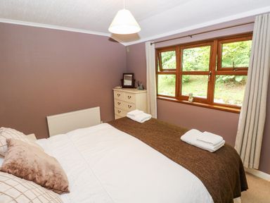 A bedroom with a bed with pillows and folded towels a chest of drawers and a window with curtains at The Beeches in Narberth