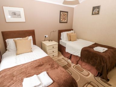 A bedroom with two single beds a bedside table and three framed pictures on walls at The Beeches in Narberth