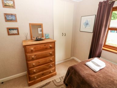 A bedroom with a wooden chest of drawers a mirror wall art a wardrobe a window with curtains and a bed with towels on it at The Beeches in Narberth