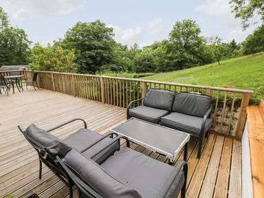 An outdoor wooden deck with black cushioned seating and a table overlooking a grassy area with trees at The Beeches in Narberth