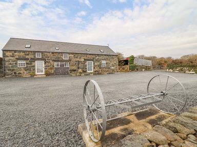A stone building with multiple windows and doors on a large gravel area with metal farm equipment at Ysgybor Yd in Chwilog near Criccieth