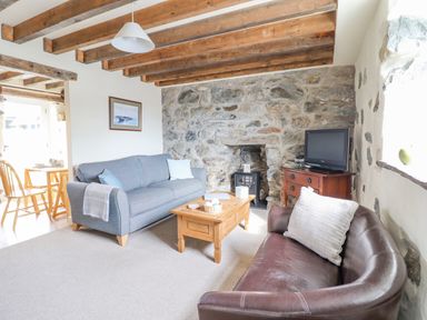A living room with a blue sofa brown chair wooden coffee table and a television at Ysgybor Yd in Chwilog near Criccieth