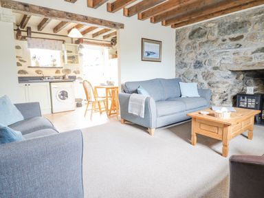 A living room with two gray sofas a wooden coffee table and a stone wall next to a kitchen and dining area at Ysgybor Yd in Chwilog near Criccieth