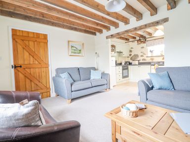 A living room with sofas and a coffee table connected to a kitchen with wooden ceiling beams at Ysgybor Yd in Chwilog near Criccieth