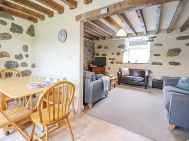 A living room with sofas and a television next to a dining area with a wooden table and chairs at Ysgybor Yd in Chwilog near Criccieth