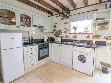 A kitchen with white cabinets wooden beams a refrigerator oven washing machine and stone walls at Ysgybor Yd in Chwilog near Criccieth