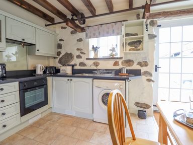 A kitchen with a wooden chair stone walls and ceiling beams at Ysgybor Yd in Chwilog near Criccieth