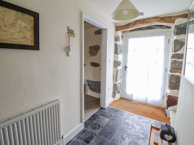 A hallway with a stone framed door a coat hook a radiator a map on the wall and a lamp at Ysgybor Yd in Chwilog near Criccieth