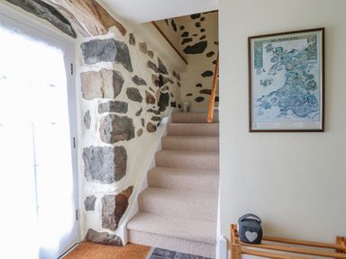 A staircase with beige carpet and stone wall next to a door and a framed map on the wall at Ysgybor Yd in Chwilog near Criccieth