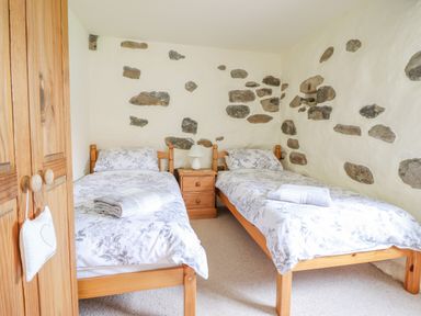 A bedroom with two single beds wooden nightstand and exposed stone walls at Ysgybor Yd in Chwilog near Criccieth