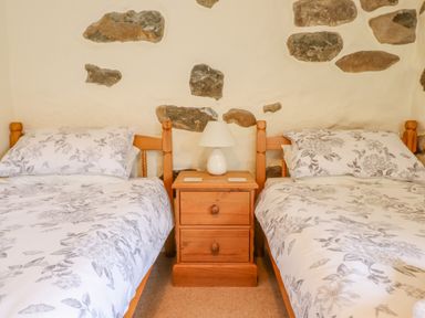 A bedroom with two single beds and a wooden nightstand with a lamp between them at Ysgybor Yd in Chwilog near Criccieth