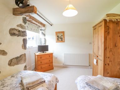 A bedroom with two beds a wooden wardrobe a wooden chest of drawers and a window at Ysgybor Yd in Chwilog near Criccieth