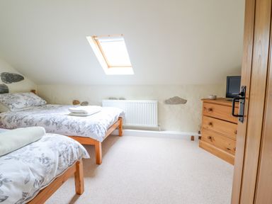 A bedroom with two beds under a skylight and a wooden dresser with a television at Ysgybor Yd in Chwilog near Criccieth