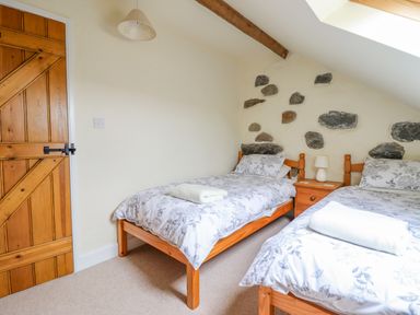 A bedroom with two single beds a wooden door and a nightstand at Ysgybor Yd in Chwilog near Criccieth