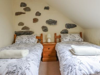 A bedroom with two single beds with floral bedding and a wooden nightstand with a lamp at Ysgybor Yd in Chwilog near Criccieth