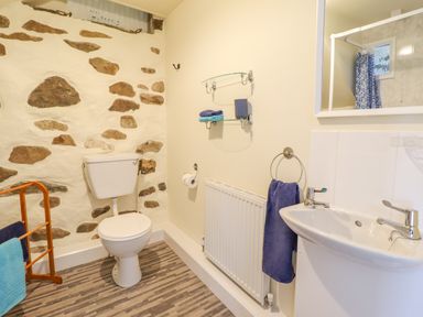 A bathroom with a toilet sink radiator towels and stone accent wall at Ysgybor Yd in Chwilog near Criccieth
