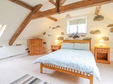 A bedroom with wooden bed and furniture under exposed wooden beams at Ysgybor Yd in Chwilog near Criccieth