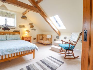 A bedroom with a wooden bed and crib a rocking chair beside a skylight window at Ysgybor Yd in Chwilog near Criccieth