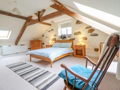 A bedroom with wooden bed and bedside tables under exposed wooden beams at Ysgybor Yd in Chwilog near Criccieth