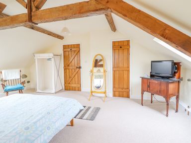 A bedroom with wooden beams white walls a bed rocking chair freestanding mirror wardrobe and a TV on a wooden cabinet at Ysgybor Yd Chwilog near Criccieth