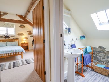 A bedroom with wooden bed and nightstand next to a bathroom with sink and towel rack at Ysgybor Yd in Chwilog near Criccieth