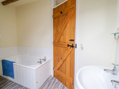 A bathroom with a bathtub and a wooden door near a sink at Ysgybor Yd in Chwilog near Criccieth