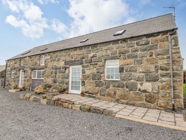A stone building with multiple windows and two white doors surrounded by gravel at Ysgybor Yd in Chwilog near Criccieth
