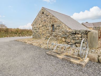 A stone building with a metal bike rack and gravel road at Ysgybor Yd in Chwilog near Criccieth