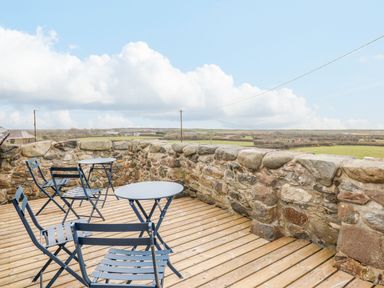 An outdoor terrace with blue metal tables and chairs and a stone wall at Ysgybor Yd in Chwilog near Criccieth