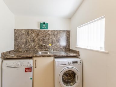 A laundry room with a washing machine dishwasher sink and countertop at Gardeners Cottage Belford near Bamburgh