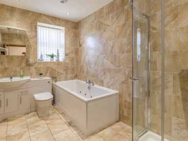 A bathroom with a white bathtub shower enclosure toilet and sink with a mirror and window at Gardener's Cottage Belford near Bamburgh