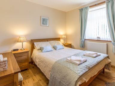 A bedroom with a double bed two bedside tables lamps a window with curtains and wooden floor at Gardeners Cottage Belford near Bamburgh