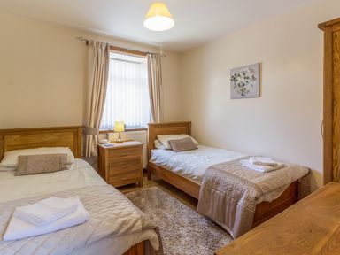 A bedroom with two single beds a nightstand with lamp and a window at Gardeners Cottage Belford near Bamburgh