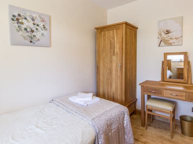 A bedroom with a single bed a wooden wardrobe a dressing table and stool with wall art at Gardeners Cottage in Belford near Bamburgh