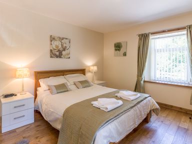 A bedroom with a double bed two bedside tables with lamps folded towels on the bed and a window with curtains at Gardener's Cottage in Belford near Bamburgh