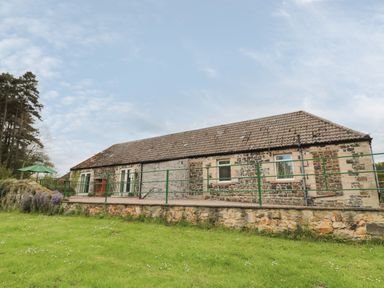 A stone building with tiled roof and green railing on a grassy lawn at Gardeners Cottage in Belford near Bamburgh