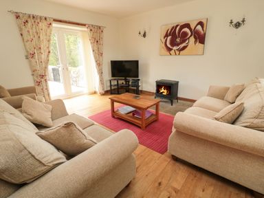 A living room with two beige sofas a wooden coffee table a red rug a wood stove and a television at Gardeners Cottage in Belford near Bamburgh