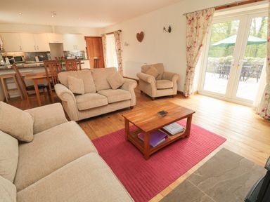A living room with beige sofas a wooden coffee table on a red rug and a kitchen area in the background at Gardeners Cottage in Belford near Bamburgh