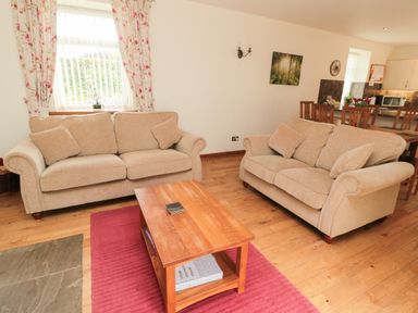 A living room with two beige sofas and a wooden coffee table on a red rug at Gardener's Cottage Belford near Bamburgh