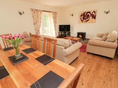 A living room with sofas a television a fireplace and a dining table with flowers at Gardener's Cottage Belford near Bamburgh