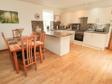 A kitchen with a wooden dining table and chairs and white cabinets with appliances at Gardeners Cottage Belford near Bamburgh