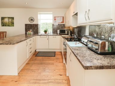 A kitchen with white cabinets and brown countertops with appliances and a window at Gardener's Cottage in Belford near Bamburgh