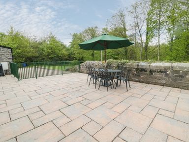 A patio with a table chairs and a green umbrella next to a stone wall and green fence at Gardeners Cottage Belford near Bamburgh