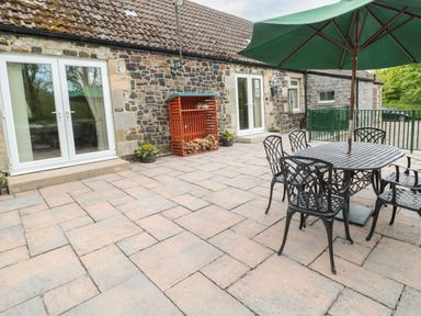 A stone patio with a metal table and chairs under a green umbrella outside a stone building at Gardeners Cottage Belford near Bamburgh