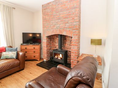 A living room with a brick fireplace a wood stove leather sofas a TV on a wooden cabinet and a side table with a lamp at Lightkeeper House in Amble-by-the-Sea
