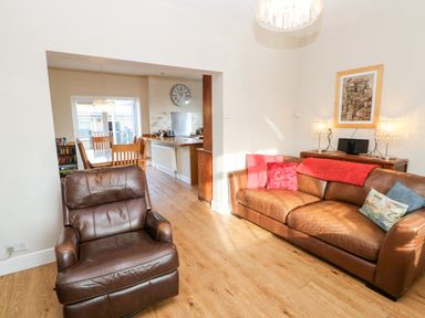 A living room with a brown leather chair and sofa with pillows next to a wooden dining table at Lightkeeper House in Amble-by-the-Sea