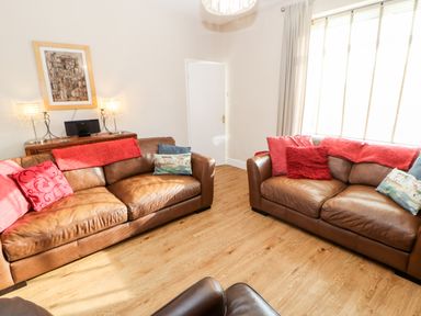 A living room with two brown leather sofas with cushions a wooden floor and a sideboard with lamps at Lightkeeper House in Amble-by-the-Sea