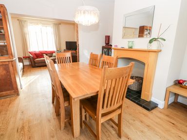 A dining room with wooden table and chairs next to a fireplace and a living area with brown sofas at Lightkeeper House in Amble-by-the-Sea